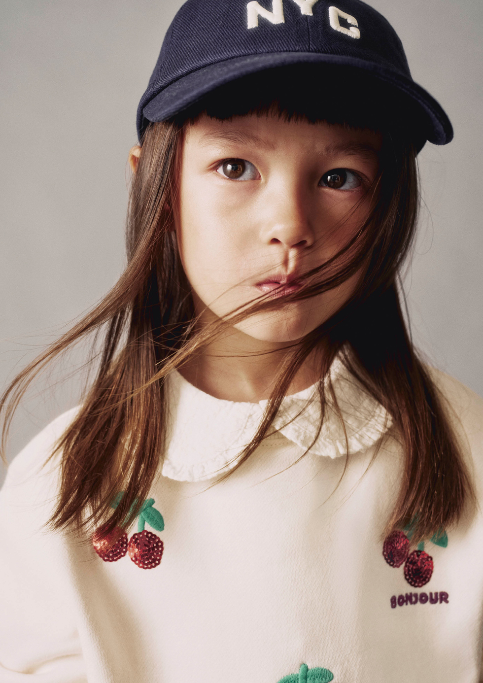 Model wearing a navy cap and a cream sweatshirt with embroidered cherries from H&M.