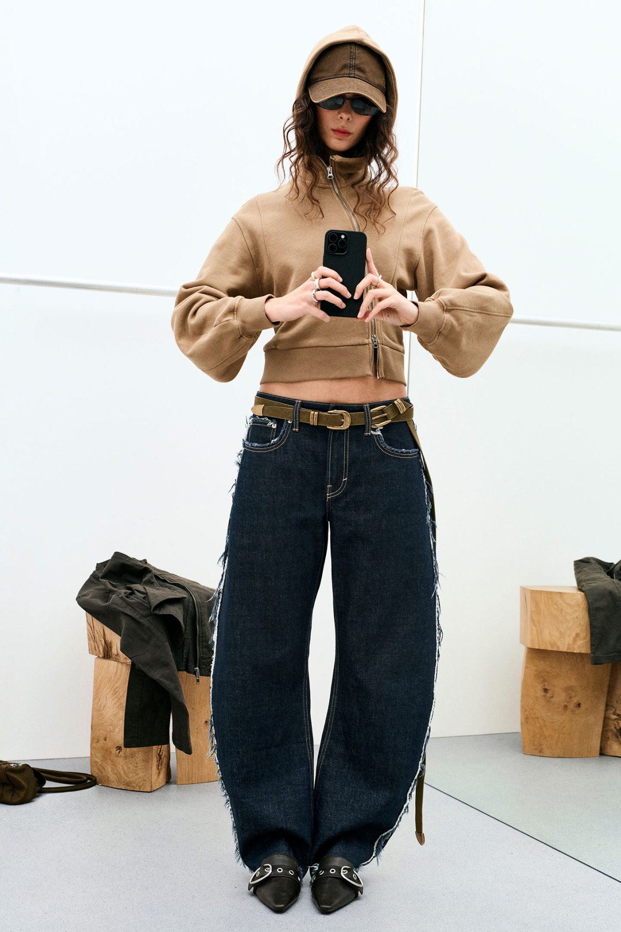 Model in tan faux-fur coat leans across a glass table; clock and filing cabinets behind.